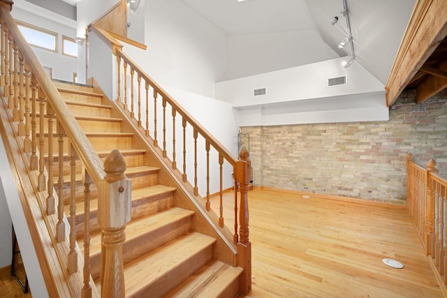 stairs featuring track lighting, hardwood / wood-style flooring, and high vaulted ceiling