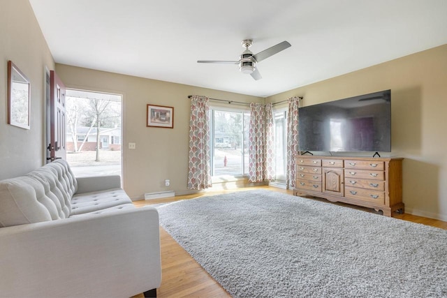 living room featuring baseboard heating, ceiling fan, plenty of natural light, and light hardwood / wood-style flooring