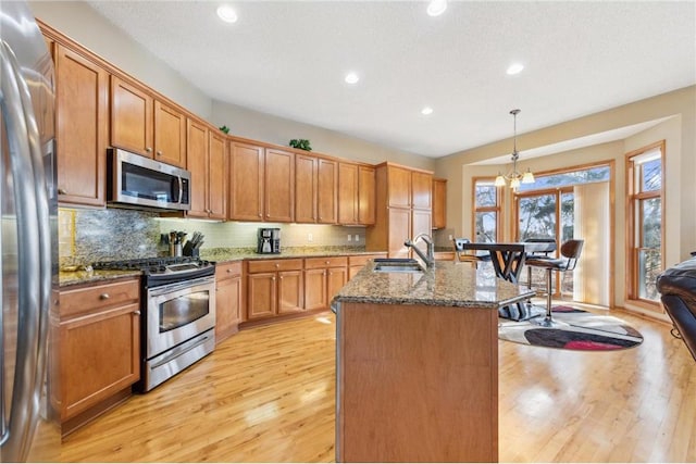 kitchen with sink, hanging light fixtures, stainless steel appliances, an island with sink, and stone countertops