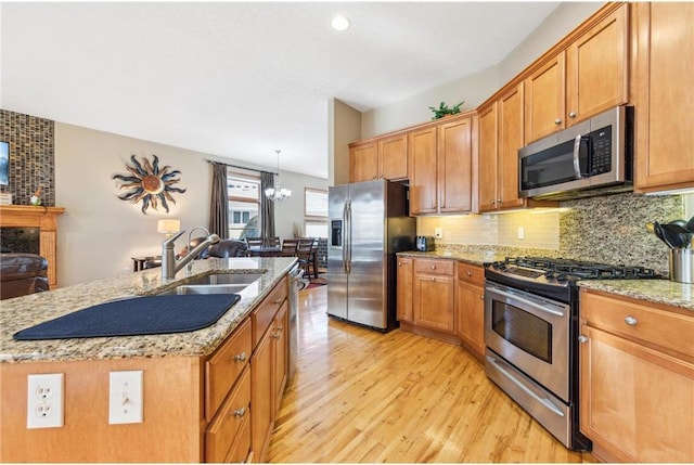 kitchen featuring sink, appliances with stainless steel finishes, an inviting chandelier, light hardwood / wood-style floors, and a center island with sink