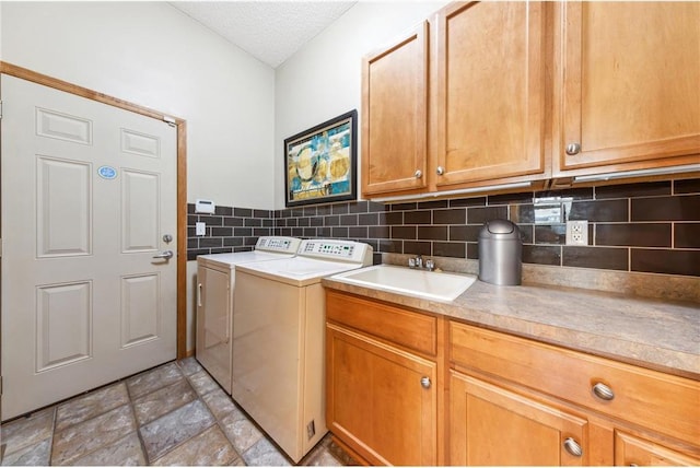 clothes washing area featuring sink, washing machine and dryer, cabinets, and a textured ceiling