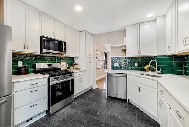 kitchen with tasteful backsplash, appliances with stainless steel finishes, sink, and white cabinets