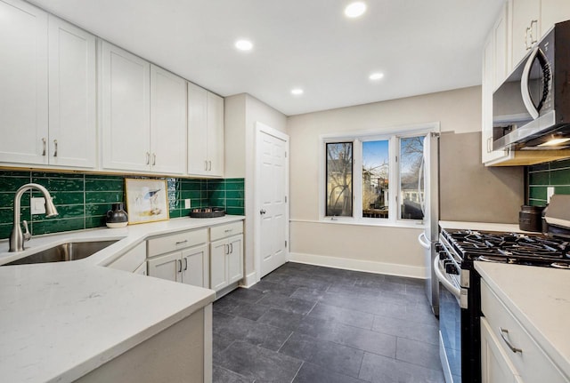 kitchen with sink, white cabinetry, stainless steel appliances, light stone countertops, and backsplash