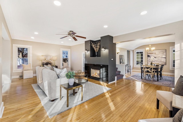 living room featuring a fireplace, ceiling fan with notable chandelier, and light hardwood / wood-style flooring