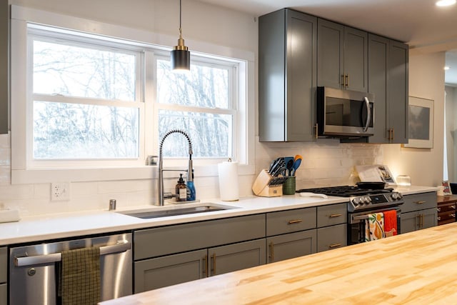 kitchen featuring pendant lighting, sink, tasteful backsplash, gray cabinets, and stainless steel appliances