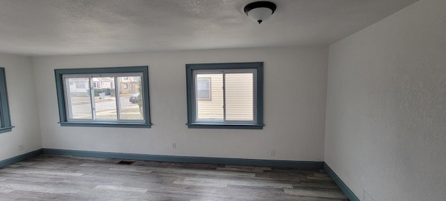 spare room with a wealth of natural light, a textured ceiling, and hardwood / wood-style floors