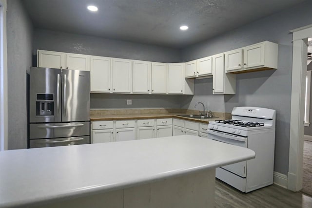 kitchen featuring white range with gas stovetop, white cabinets, stainless steel fridge with ice dispenser, and sink