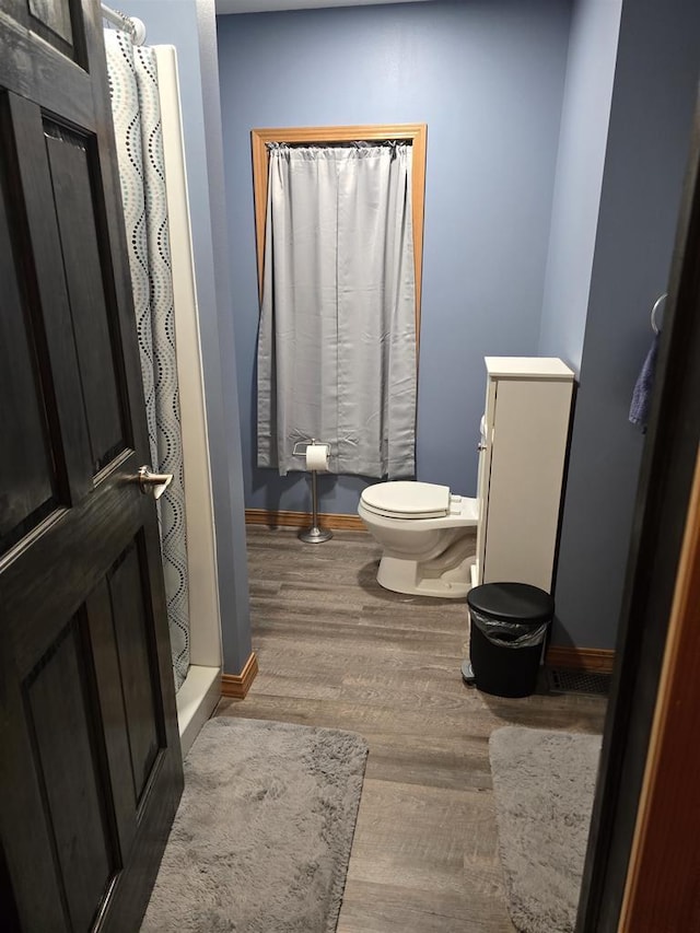 bathroom featuring toilet, curtained shower, and wood-type flooring