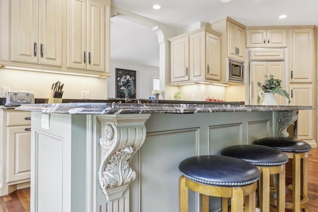 kitchen featuring dark stone counters, stainless steel microwave, a breakfast bar area, and wood-type flooring