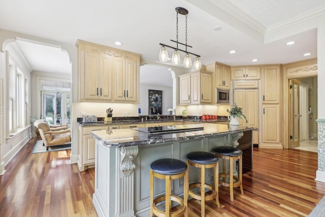 kitchen featuring a center island, stainless steel microwave, wood-type flooring, dark stone countertops, and ornamental molding