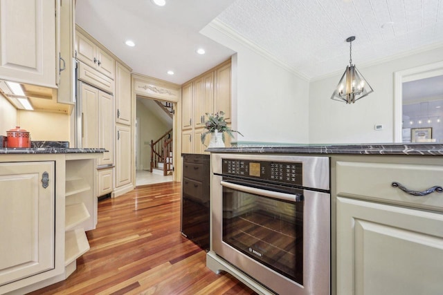 kitchen with decorative light fixtures, cream cabinets, crown molding, and stainless steel oven