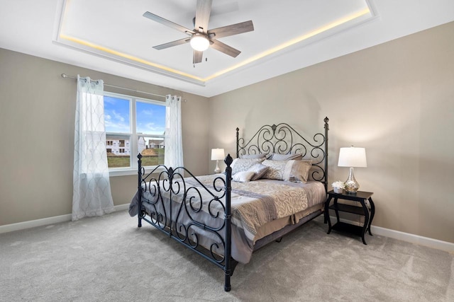 carpeted bedroom with ceiling fan and a raised ceiling