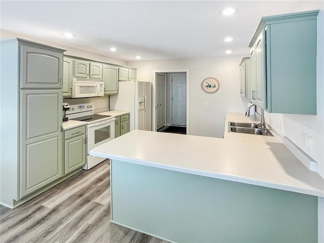 kitchen with light wood-type flooring, sink, white appliances, and kitchen peninsula