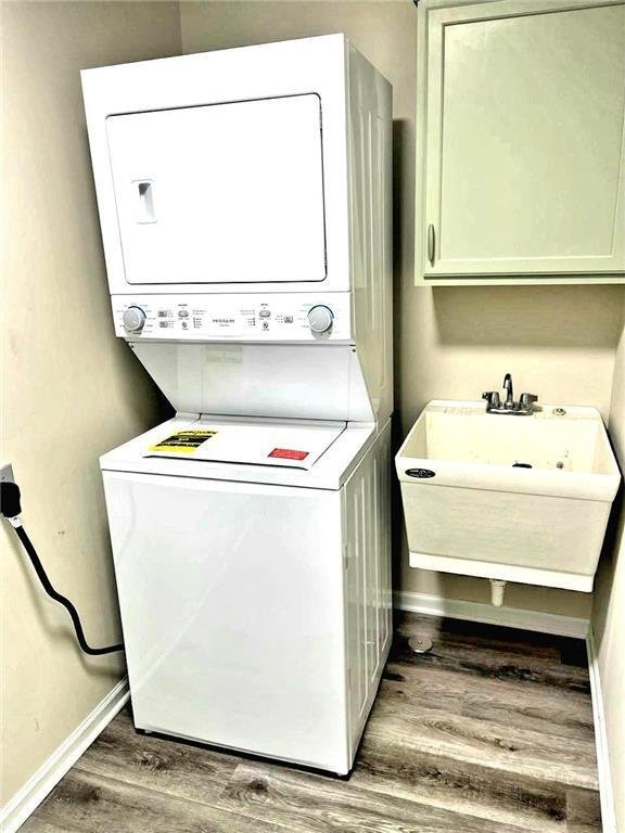 washroom with stacked washer / drying machine, hardwood / wood-style flooring, cabinets, and sink