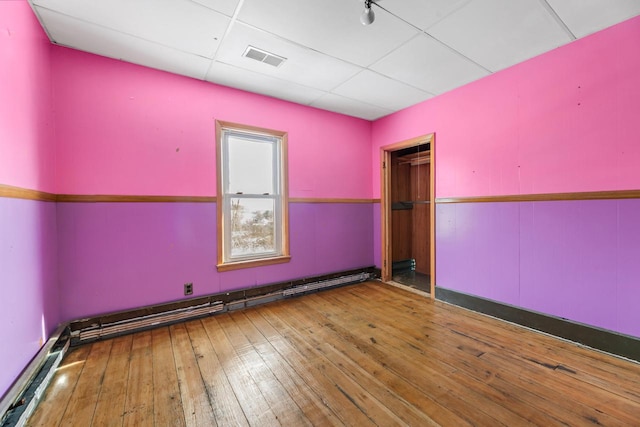 unfurnished room with wood-type flooring, a baseboard radiator, and a paneled ceiling