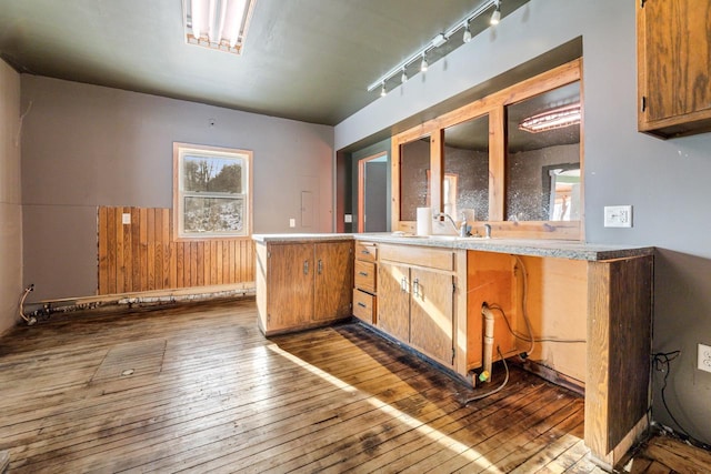 kitchen featuring hardwood / wood-style flooring, sink, kitchen peninsula, and wood walls