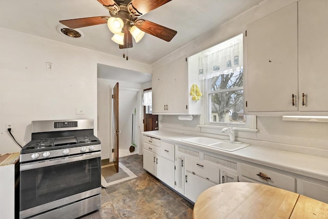 kitchen featuring ceiling fan, sink, white cabinetry, and stainless steel gas range oven