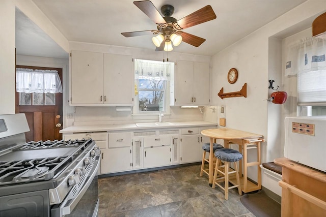 kitchen featuring ceiling fan, stainless steel range with gas cooktop, white cabinets, and sink