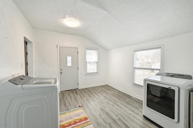 washroom with light hardwood / wood-style flooring, washing machine and dryer, and a textured ceiling