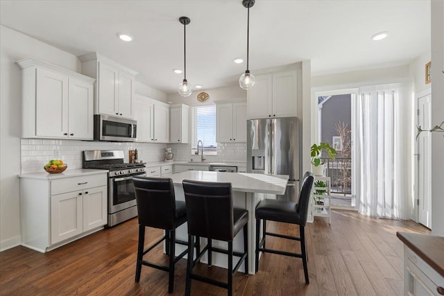 kitchen with stainless steel appliances, a kitchen island, hanging light fixtures, and white cabinets