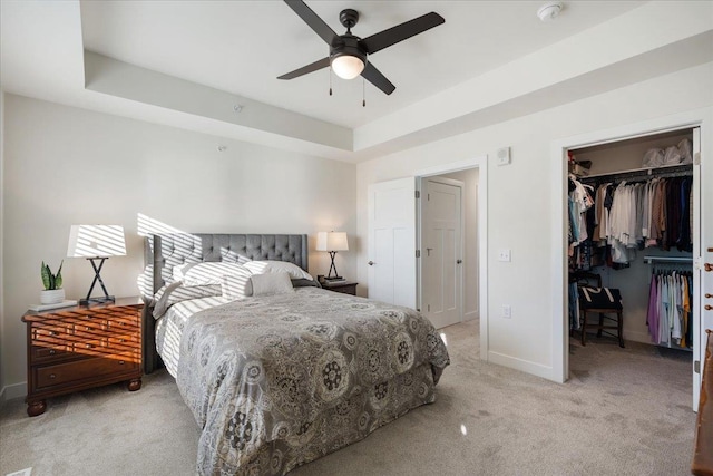 bedroom featuring a walk in closet, ceiling fan, a raised ceiling, light carpet, and a closet