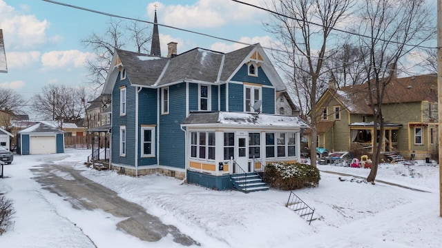 snow covered back of property with a garage, a sunroom, and an outbuilding