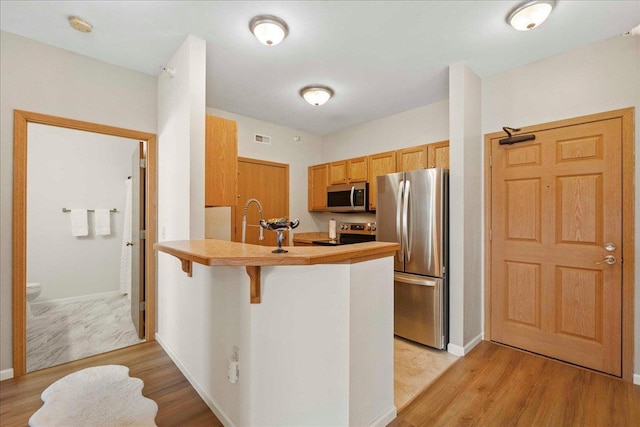 kitchen featuring appliances with stainless steel finishes, light wood-type flooring, sink, kitchen peninsula, and a breakfast bar