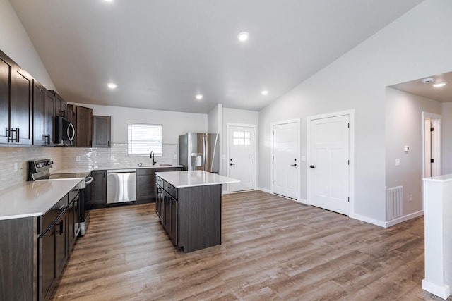 kitchen featuring appliances with stainless steel finishes, a center island, vaulted ceiling, light wood-type flooring, and dark brown cabinets