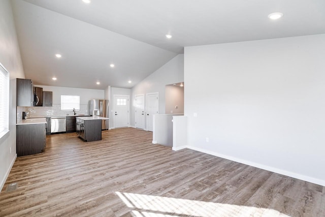 unfurnished living room with light hardwood / wood-style floors, sink, and high vaulted ceiling