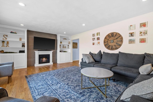 living room featuring built in shelves, a large fireplace, and light wood-type flooring