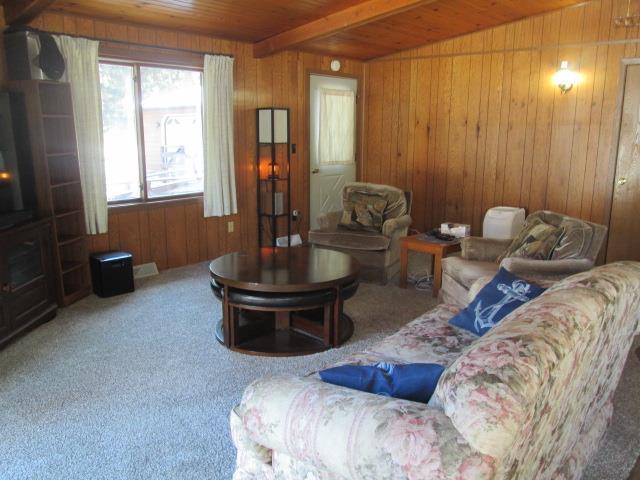 carpeted living room featuring wooden ceiling, beamed ceiling, and wood walls