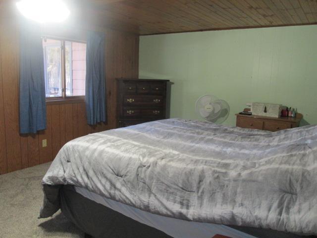 carpeted bedroom featuring wood ceiling and wooden walls