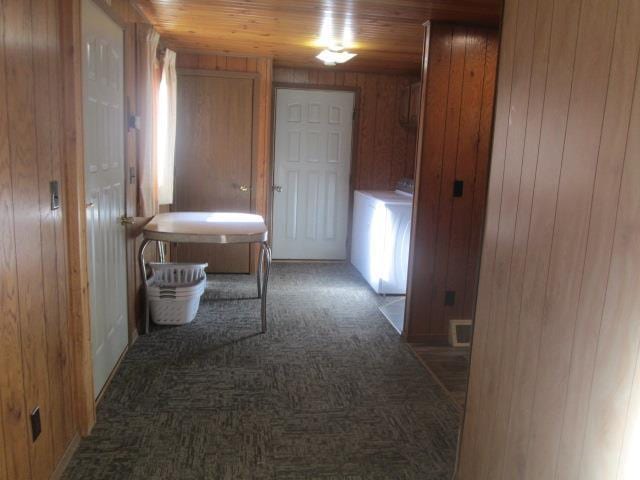 hallway with dark colored carpet, wood ceiling, and wood walls