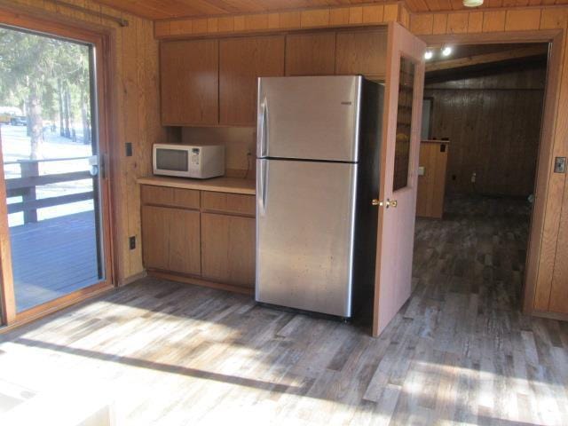 kitchen featuring hardwood / wood-style floors, wood ceiling, stainless steel fridge, and wooden walls