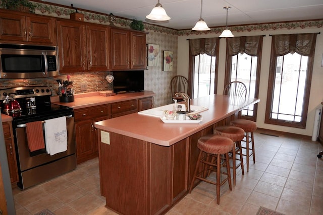 kitchen featuring pendant lighting, stainless steel appliances, a kitchen island with sink, and plenty of natural light