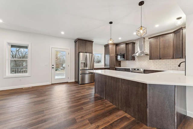 kitchen with wall chimney exhaust hood, stainless steel refrigerator with ice dispenser, backsplash, hanging light fixtures, and dark hardwood / wood-style floors