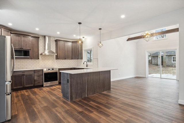 kitchen featuring wall chimney range hood, pendant lighting, dark hardwood / wood-style flooring, backsplash, and stainless steel appliances