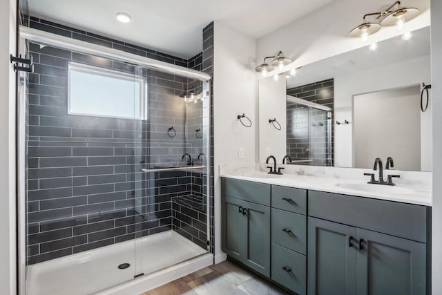full bathroom with double vanity, a sink, a shower stall, and wood finished floors