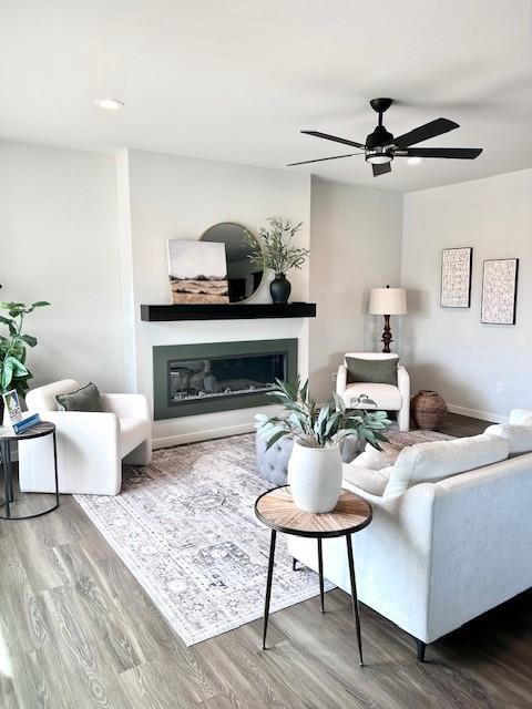 living room with baseboards, ceiling fan, a glass covered fireplace, and wood finished floors