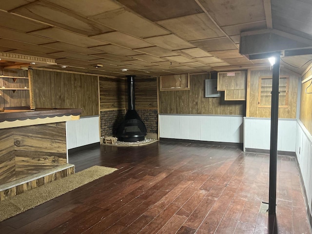 basement with electric panel, a wood stove, wooden walls, and dark hardwood / wood-style floors