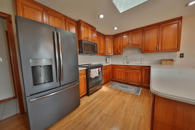 kitchen featuring a skylight, stainless steel refrigerator with ice dispenser, sink, light wood-type flooring, and range with electric stovetop