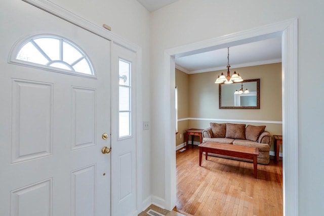 foyer entrance with hardwood / wood-style flooring, ornamental molding, and a chandelier