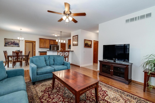 living room with ceiling fan with notable chandelier and hardwood / wood-style flooring