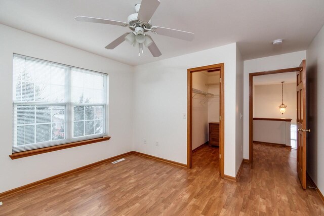 unfurnished bedroom with light hardwood / wood-style flooring, a walk in closet, a closet, and ceiling fan