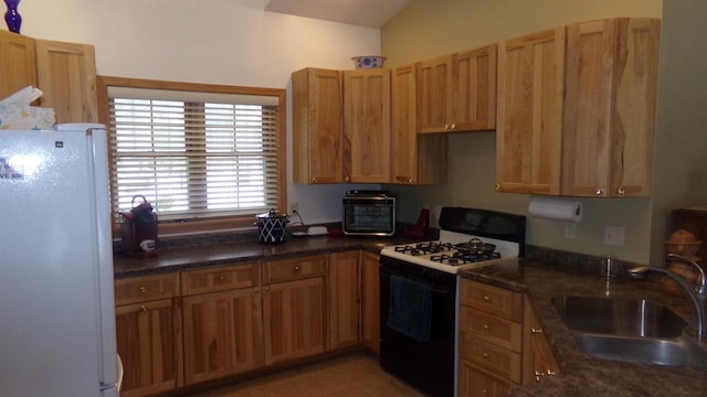 kitchen featuring sink, gas stove, dark stone counters, white refrigerator, and lofted ceiling