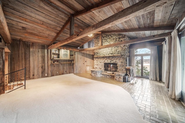 unfurnished living room with wood walls, beamed ceiling, a stone fireplace, and wood ceiling