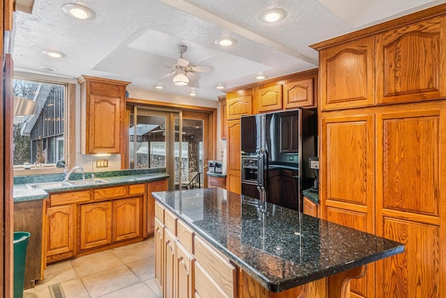 kitchen featuring a textured ceiling, sink, a kitchen island, black fridge, and light tile patterned flooring