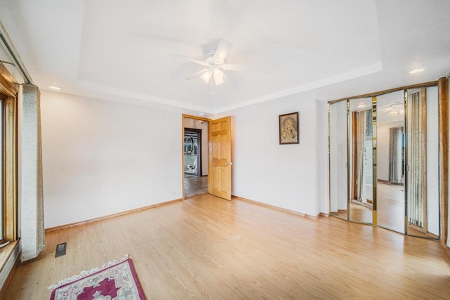 empty room featuring light wood-type flooring, ceiling fan, and a raised ceiling