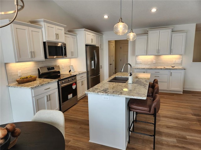 kitchen with appliances with stainless steel finishes, white cabinetry, hanging light fixtures, a kitchen island with sink, and sink