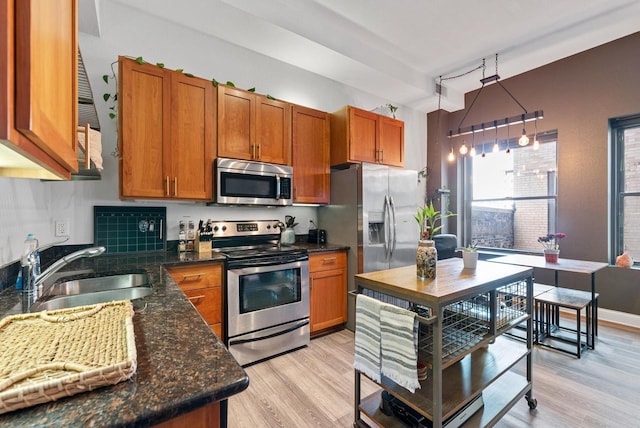 kitchen featuring sink, dark stone counters, hanging light fixtures, light hardwood / wood-style floors, and stainless steel appliances